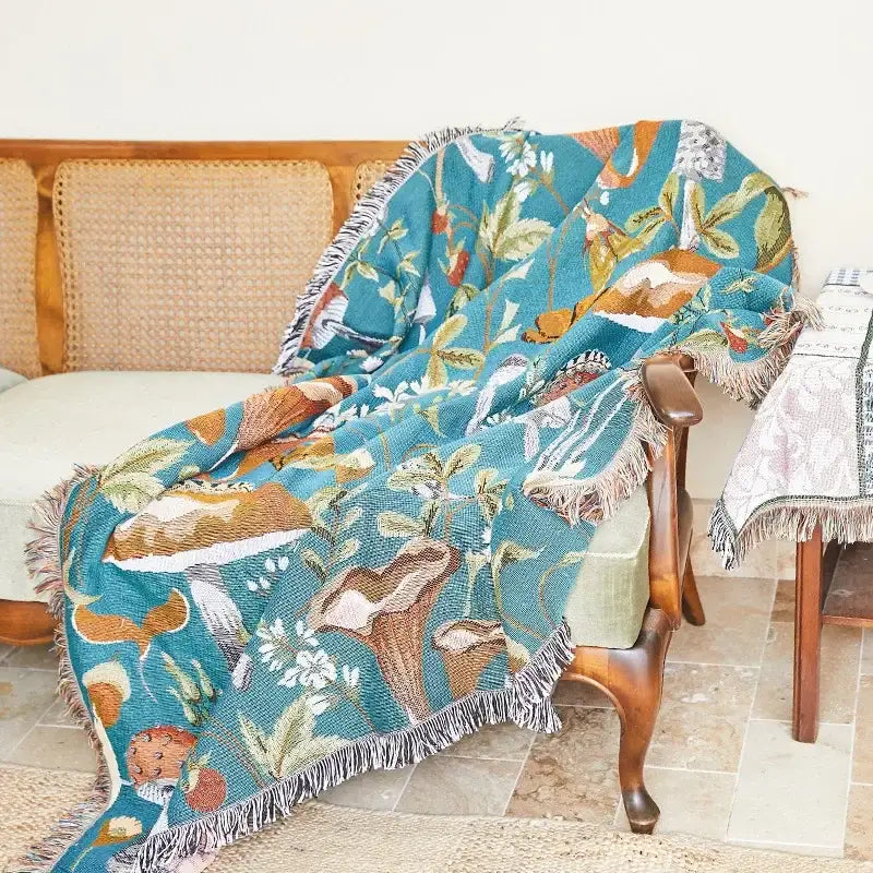 A teal woven throw blanket with fringed edges and detailed botanical wildlife pattern from decorbites bohemian classic design