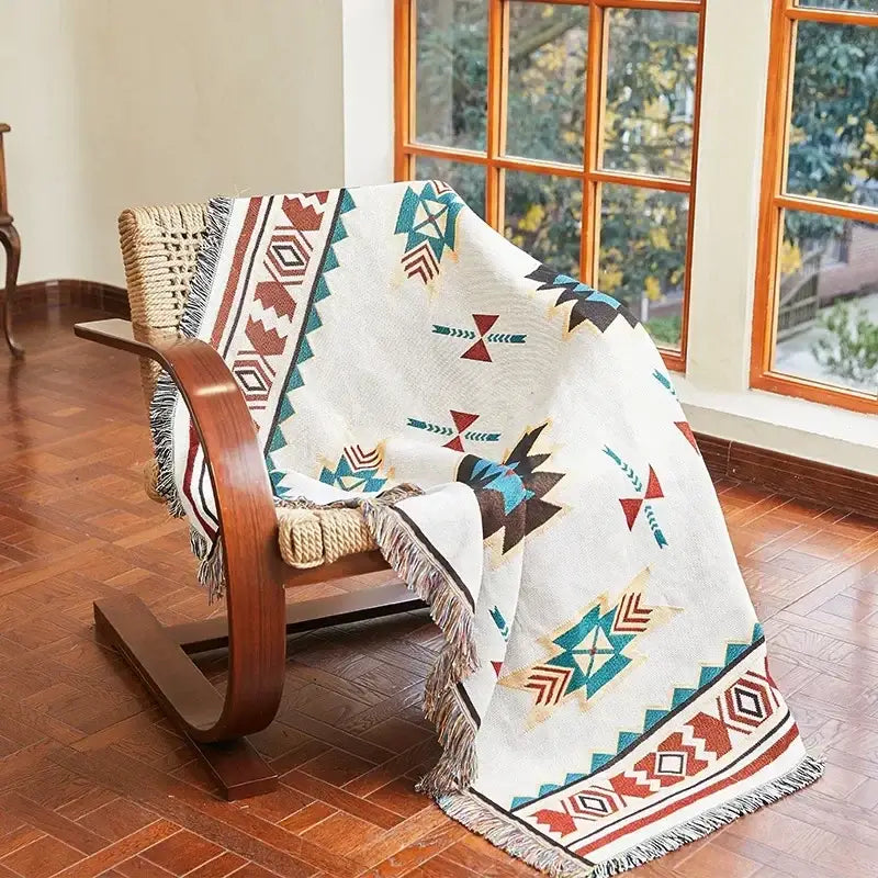 A cream-colored woven bohemian classic design thread throw blanket with teal rust black geometric patterns and fringed edges