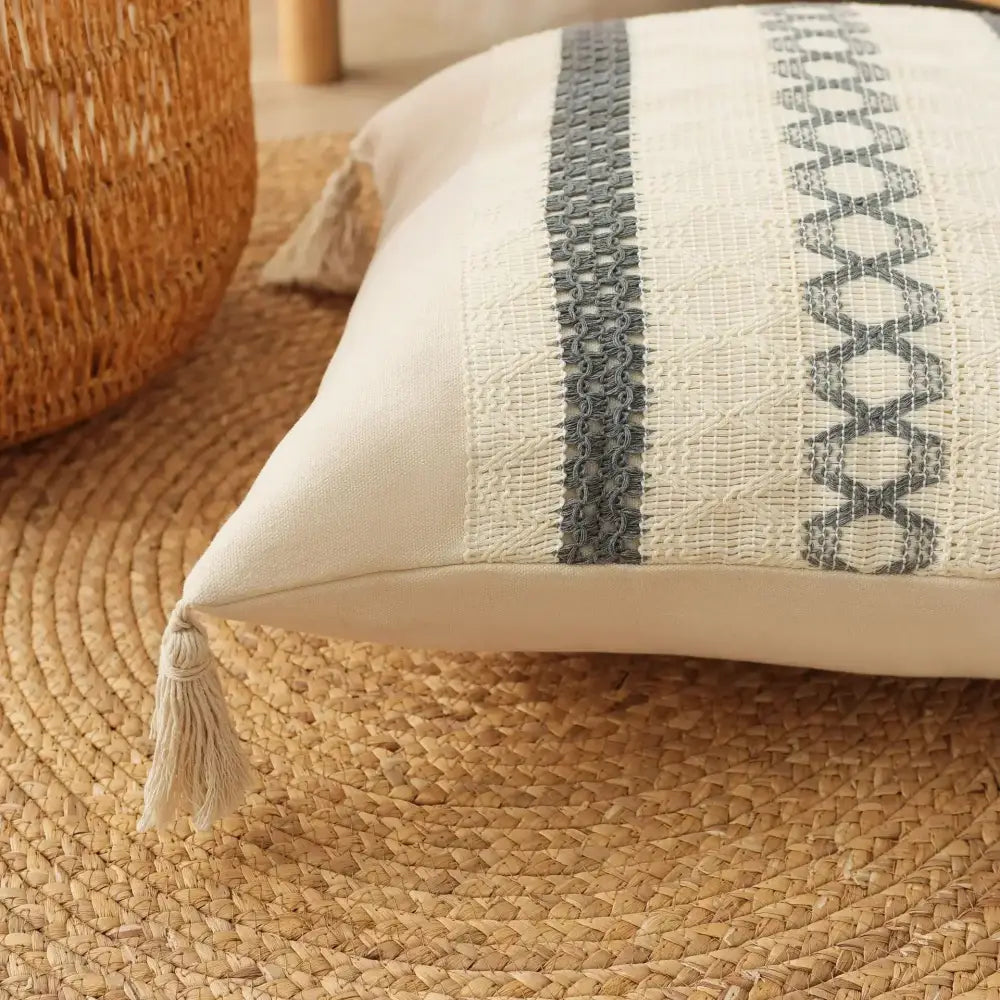 Cream-colored cushion cover with textured weave gray embroidered x-pattern and tassels decorbites bohemian tassel design