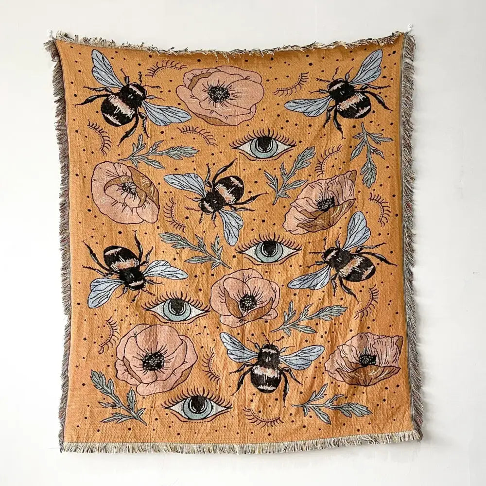 A mustard-yellow decorbites bohemian throw blanket with black-and-white bees pink poppies blue eyes and fringed edges