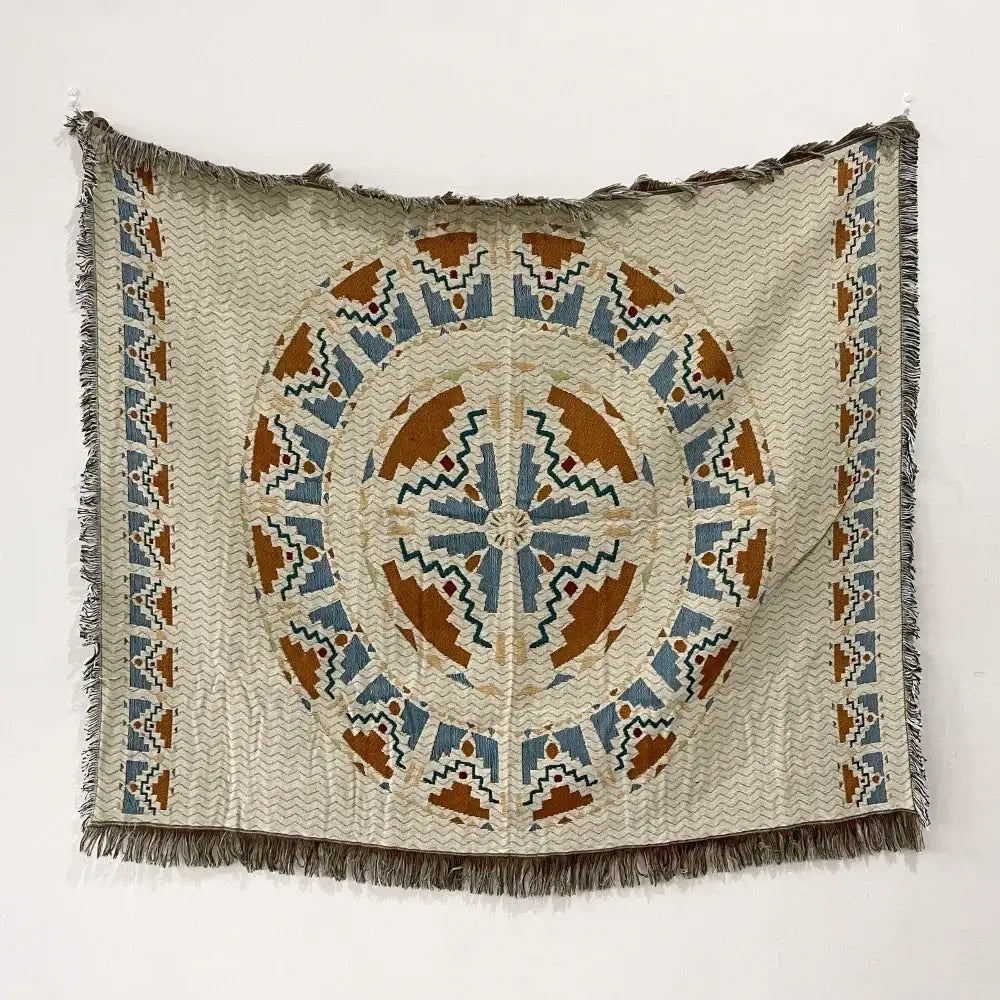Beige woven bohemian throw blanket with a central blue orange green geometric pattern and fringed edges from decorbites