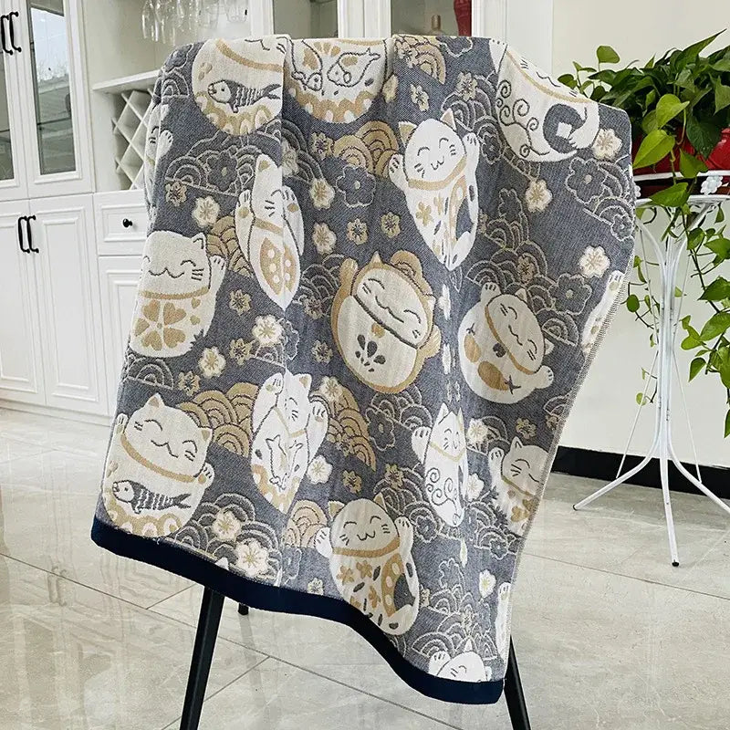 Gray cotton blanket with white beige lucky cat pattern and gold accents displayed on black chair for decorbites bohemian floral bath towel wrap