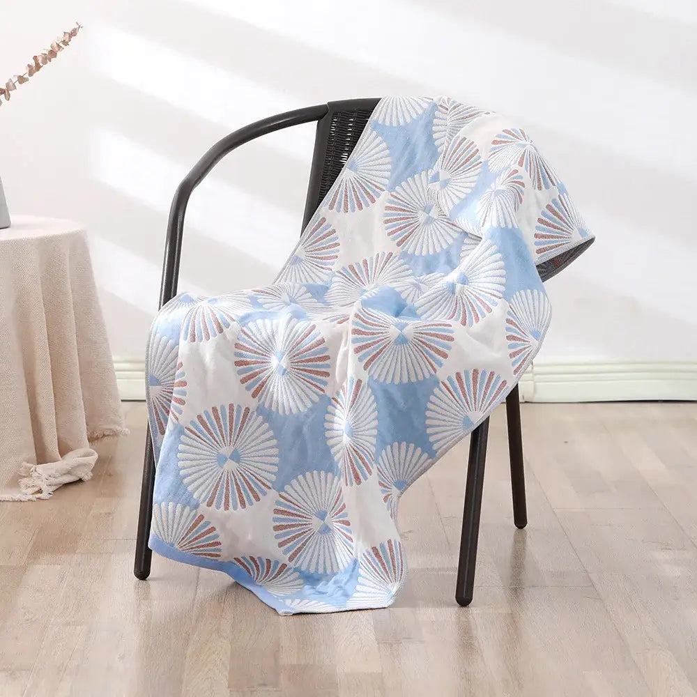 Light blue and white patterned bohemian floral cotton bath towel with muted red accents draped on black wicker chair