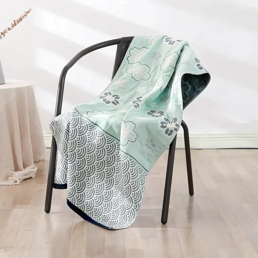 A soft mint green and gray bohemian floral cotton bath towel with dual patterns draped over a black chair by decorbites