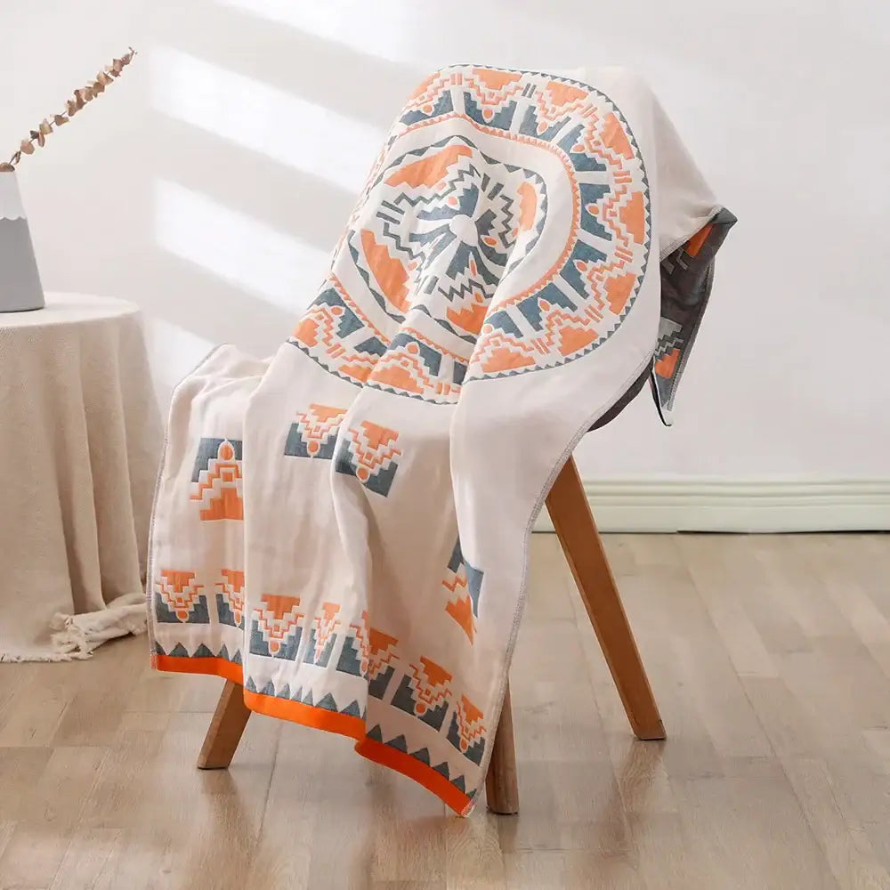 A soft cream-colored decorbites bohemian floral cotton bath towel with orange and teal geometric pattern draped on chair