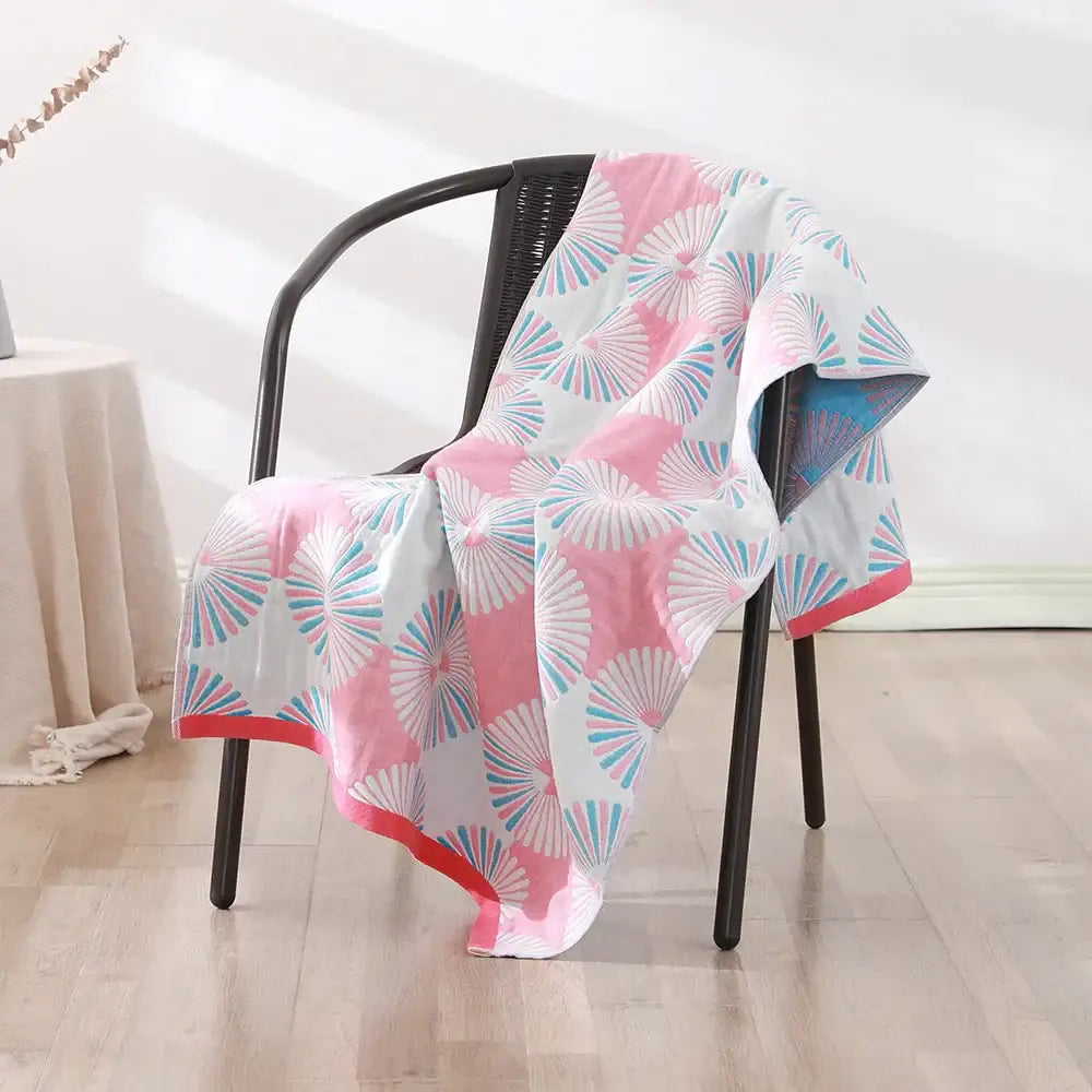 A soft white bohemian floral cotton bath towel with vibrant pink and teal fan pattern draped on a black wicker chair