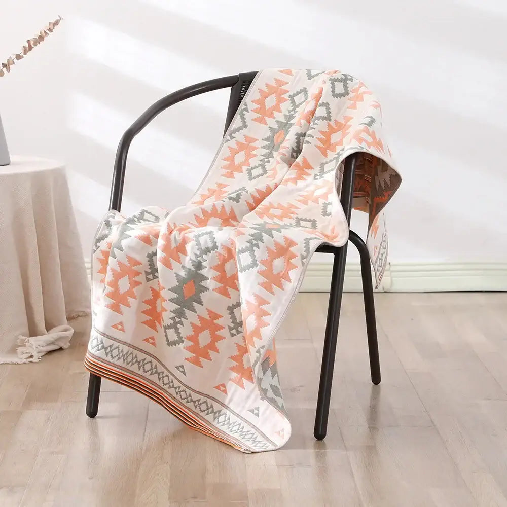 A cream-colored bohemian floral cotton bath towel with coral and gray geometric pattern draped over a black chair