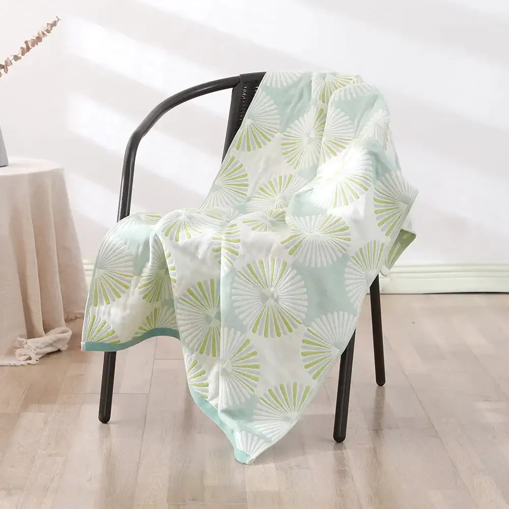 A soft mint green and white quilted decorbites bohemian floral cotton bath towel draped over a black chair