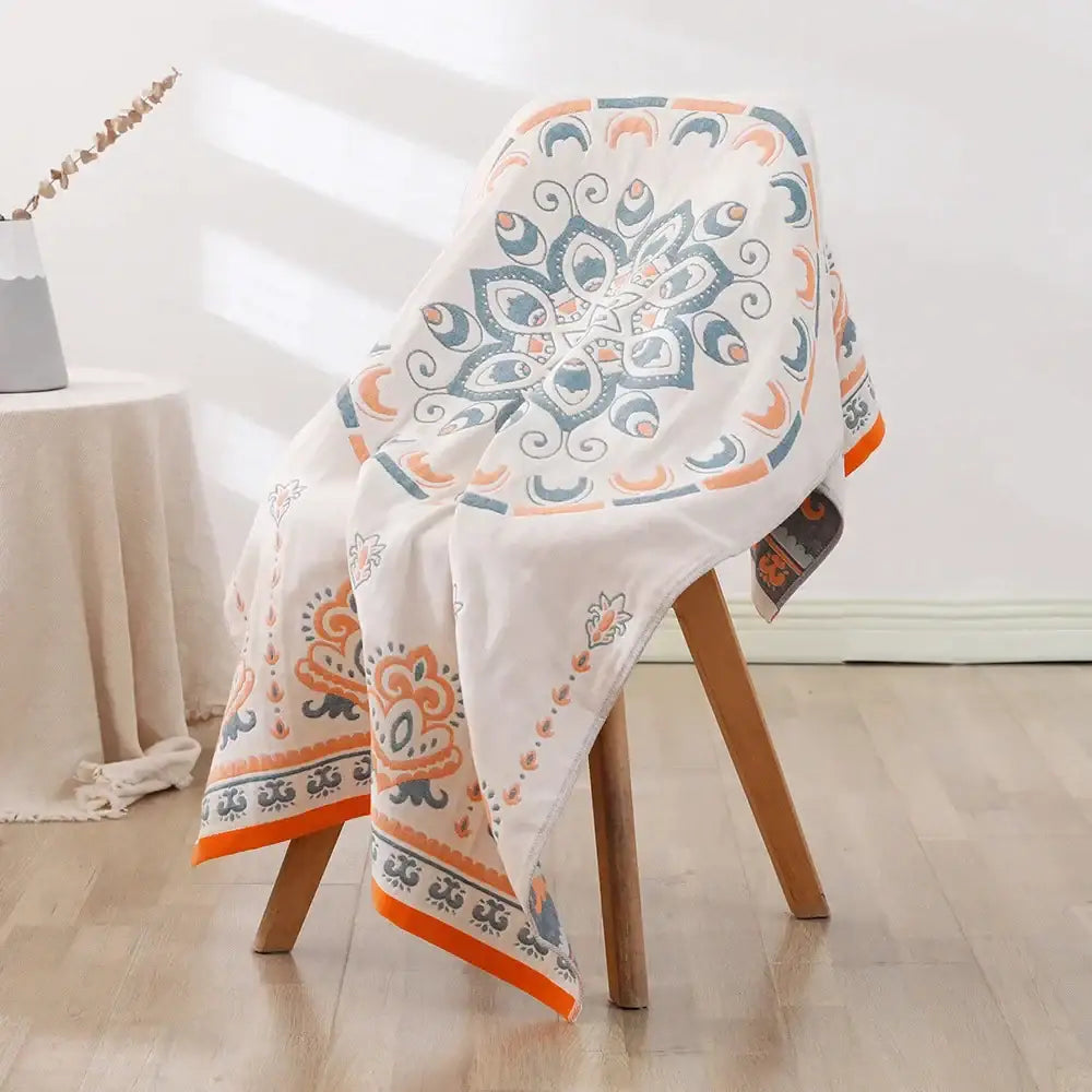 A white bohemian floral cotton bath towel with vibrant orange and teal mandala pattern draped over a wooden chair