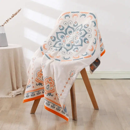 A white bohemian floral cotton bath towel with vibrant orange and teal mandala pattern draped over a wooden chair