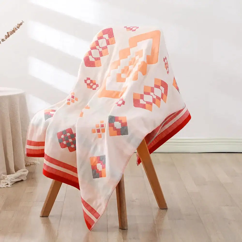 A bohemian floral cotton bath towel in white with orange red and gray geometric patterns draped over a chair