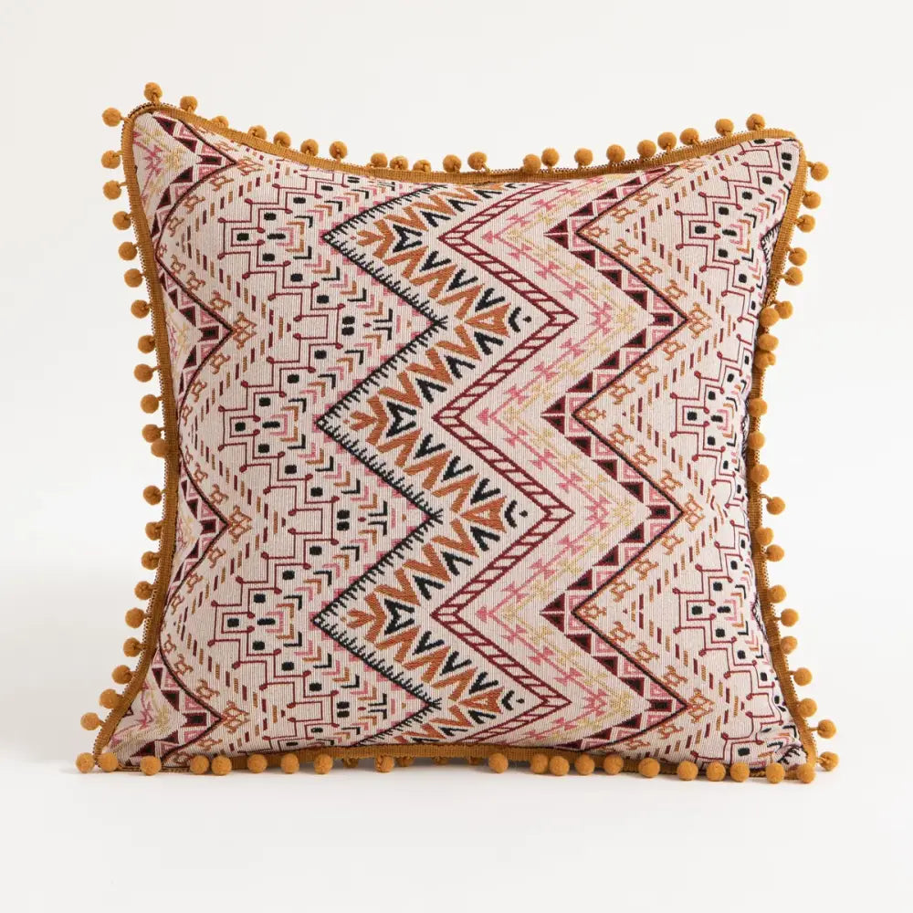 Beige square cushion cover with rust and black geometric patterns and mustard-yellow pom-poms decorbites bohemian flower