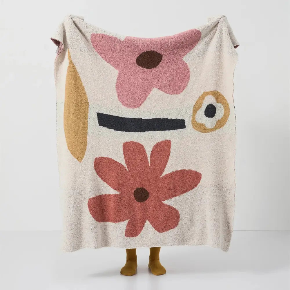 Cream-colored bohemian flower knitted throw blanket with abstract face and textured pink rust floral decorbites design
