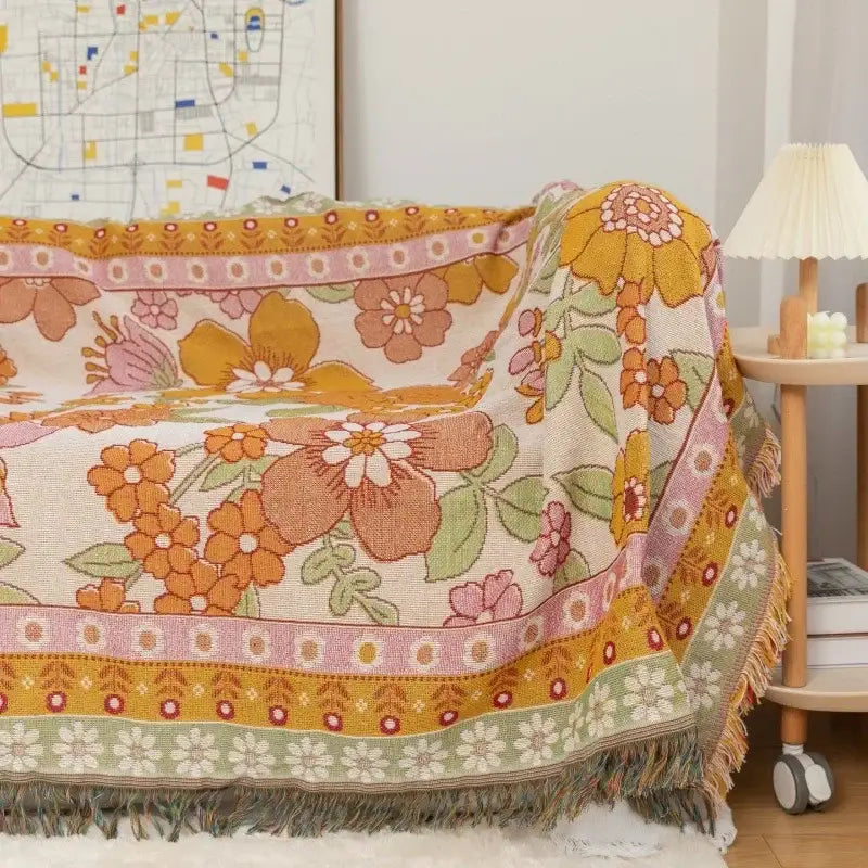 A cozy woven sofa blanket with vibrant bohemian flowers in orange pink and green featuring fringed edges decorbites bohemian flowers