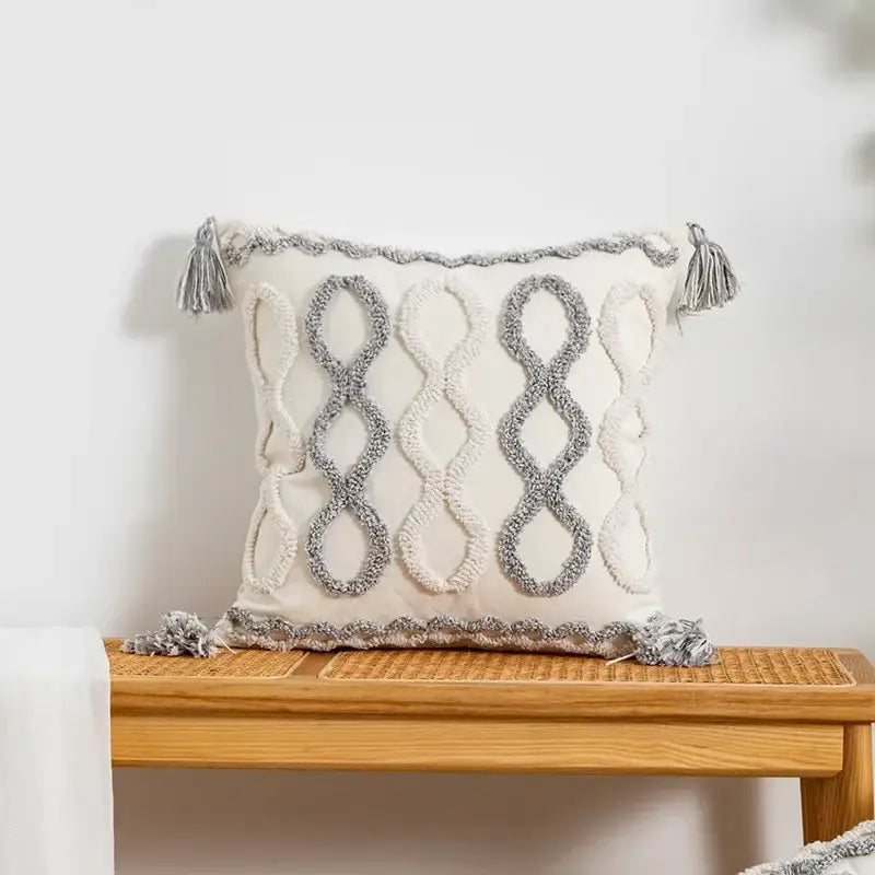 Cream-colored cushion cover with textured gray infinity symbol embroidery and tassels for decorbites geometric tufted decor