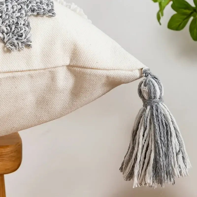 Cream-colored cushion cover with textured gray embroidered patch and matching tassel decorbites geometric tufted pillow cover