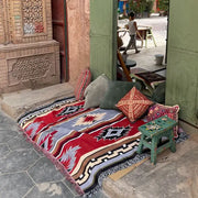 A vibrant red blue and beige decorbites bohemian knit throw blanket with geometric pattern and fringed edges on stone patio