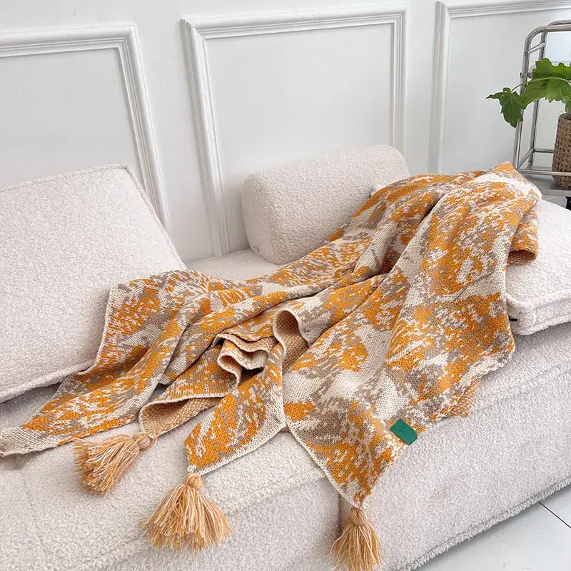 A cozy decorbites bohemian knitted blanket in warm orange beige tones with tassels for earthy bedroom decor