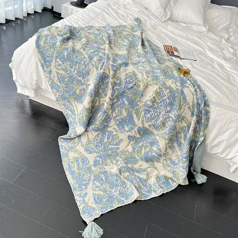 A decorbites bohemian knitted blanket in light blue and cream with an intricate leafy pattern and tassels