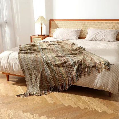 A cozy earth toned bohemian knitted blanket with multi color zigzag pattern and fringed edges for living room