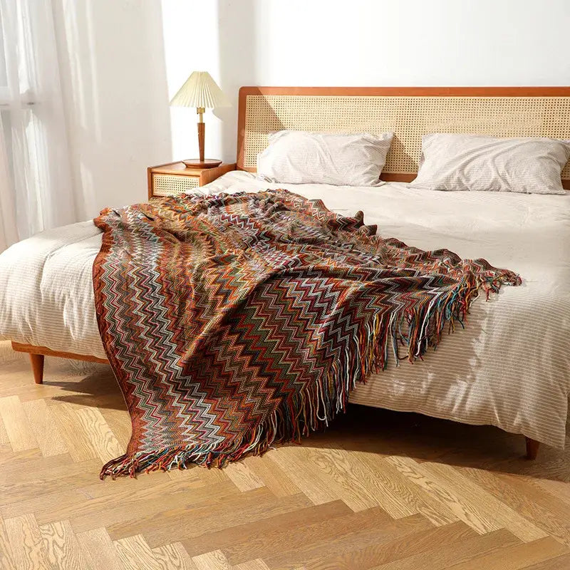 A cozy bohemian knitted blanket with multicolored zigzag pattern and fringed edges for living room use
