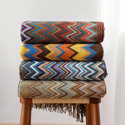 Stacked bohemian knitted blankets with vibrant multicolored zigzag patterns and fringe detailing for living room use