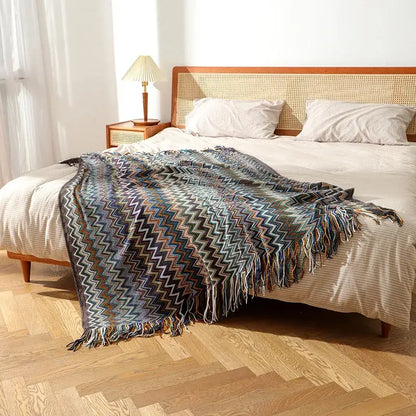 A bohemian knitted blanket with a colorful zigzag pattern in blue gray and brown and fringed edges for living room use