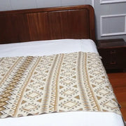 Beige and brown bohemian knitted sofa blanket with geometric pattern and woven texture draped over bed edge decorbites