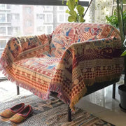 A decorbites bohemian knitted sofa cover in warm earth tones with reds blues and golds draped over a chair
