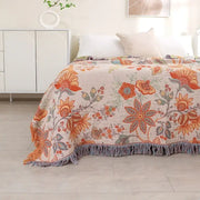 A cozy beige bohemian sofa blanket with vibrant orange and green floral patterns and soft fringe by decorbites