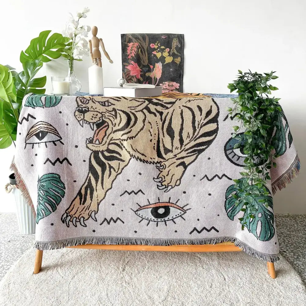 Beige woven bohemian outdoor blanket by decorbites featuring a bold gray tiger design with black stripes and green monstera leaves