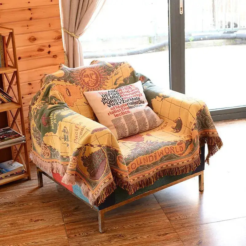 A cozy bohemian pink and red decorbites knitted cotton throw blanket with a vintage world map design and fringed edges draped on an armchair