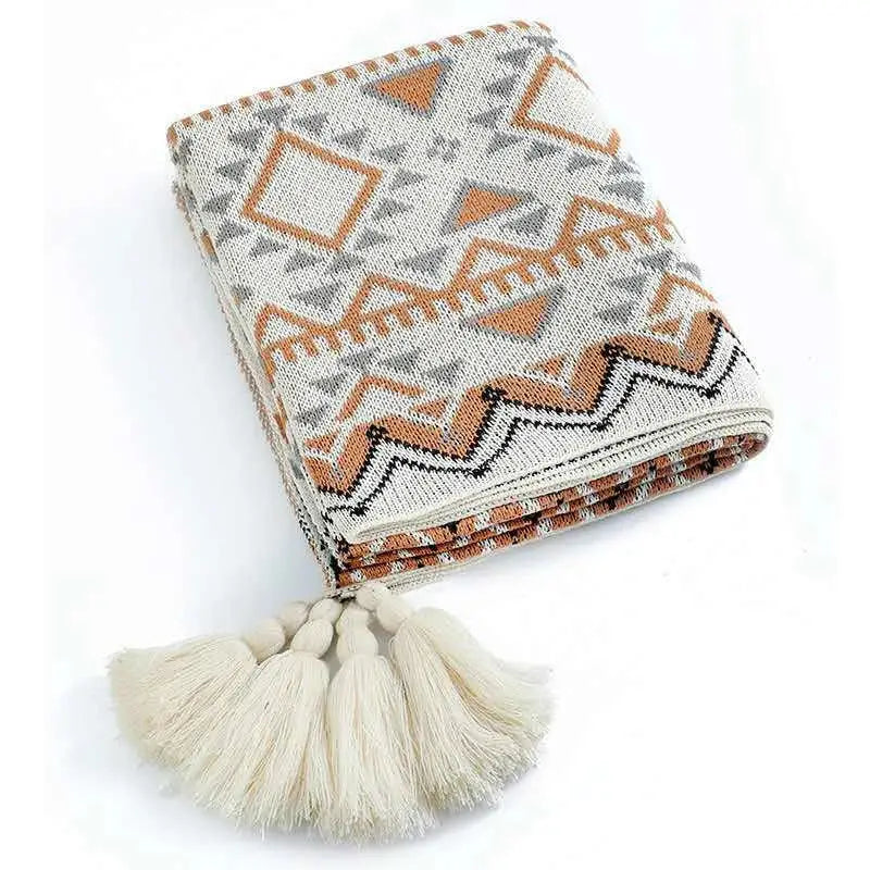 A cream cream-colored bohemian striped knit throw blanket with gray and terracotta geometric patterns and tassel fringe