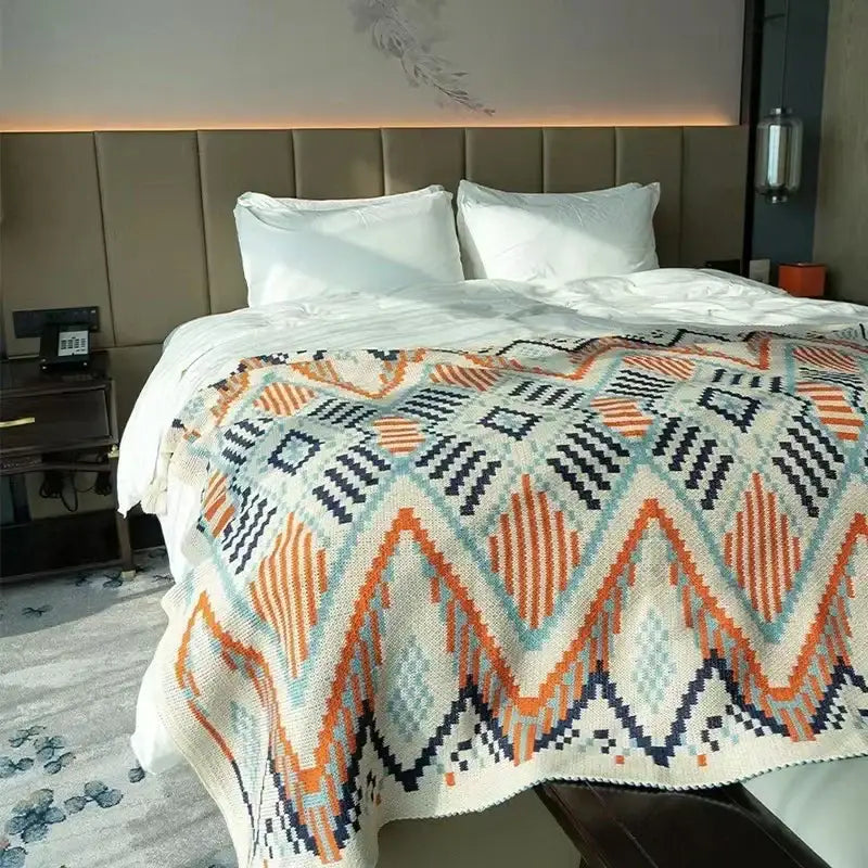 A cozy cream-colored bohemian striped knit throw blanket with bold orange navy blue and teal geometric patterns