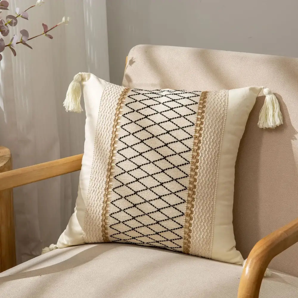 Cream-colored pillow cover with black diamond embroidery, beige woven trim, and tassels by decorbites bohemian style fringed design
