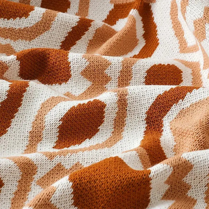 A cozy orange and white knitted bohemian winter blanket featuring a geometric pattern ideal for bedroom decor