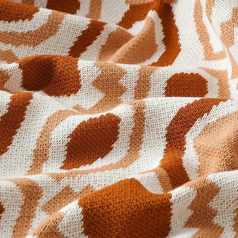 A cozy orange and white knitted bohemian winter blanket featuring a geometric pattern ideal for bedroom decor