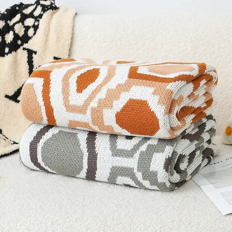 Stacked knitted Bohemian winter blankets in orange white and muted gray brown tones for decorbites bohemian winter decor