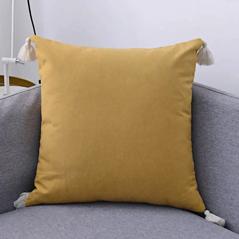 Boho beige linen pillow cover set featuring a mustard-yellow textured pillow cover with white tassels for living room sofa