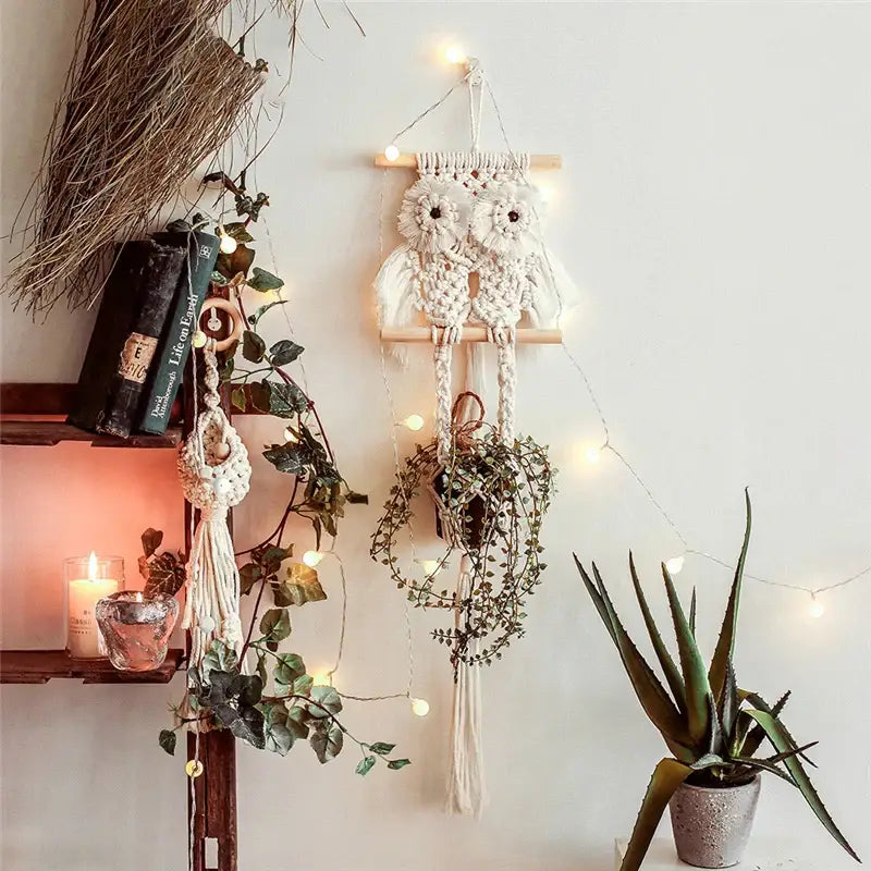 A cream-colored macrame plant hanger basket owl wall hanging with wooden dowel and tassels for boho decor
