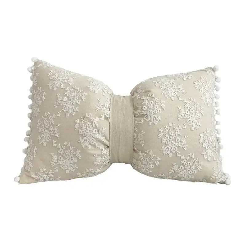Beige bow-shaped pillow cover with white floral embroidery and pom-pom trim made of linen cotton for living room decor