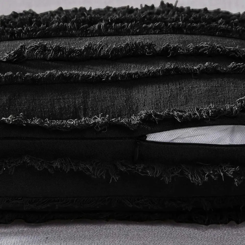 Black distressed fabric pillow cover with tassel striped design and frayed edges featuring a white zipper pull for home decor