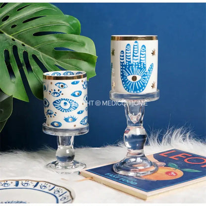 Two bright eyes ceramic candle holders with blue eye motifs and gold rims on clear glass stems for decorbites bright eyes decor