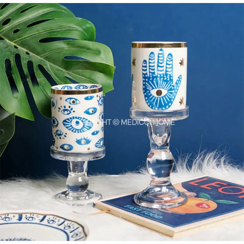 Two bright eyes ceramic candle holders with blue eye motifs and gold rims on clear glass stems for decorbites bright eyes decor