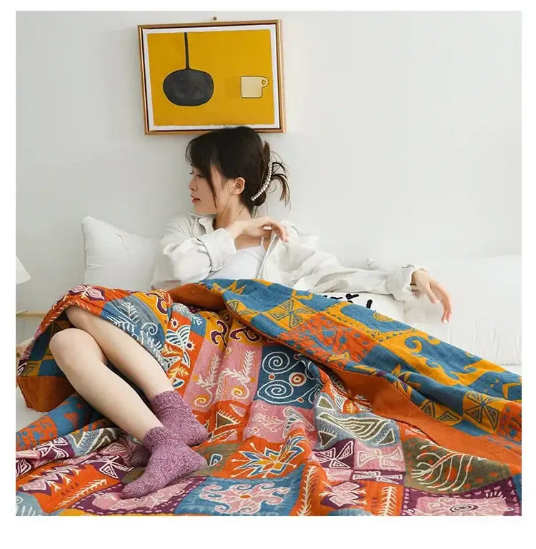 A decorbites boho cotton blanket with bold orange blue and pink geometric patterns draped over a lap for bedroom decor