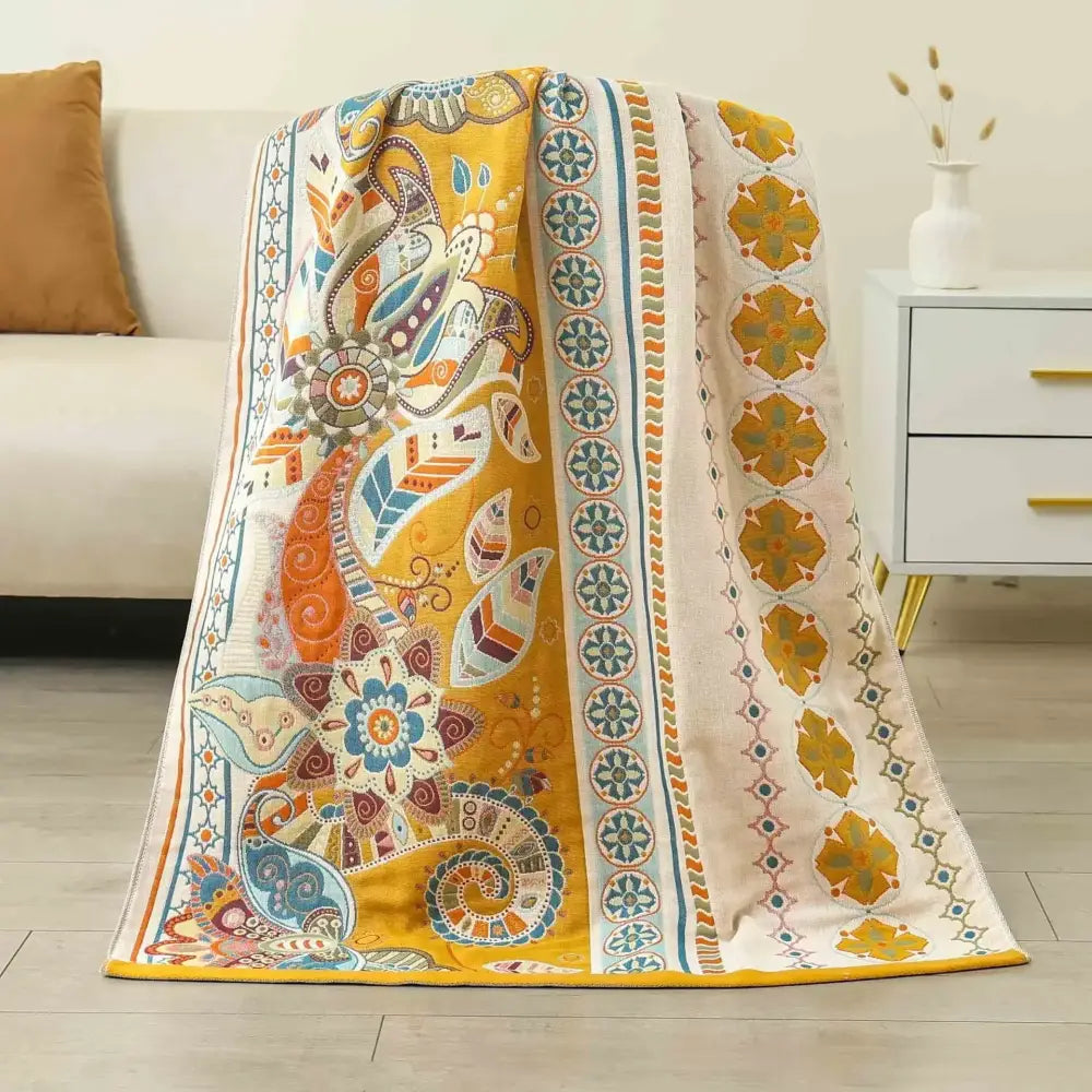 A vibrant decorbites boho cotton gauze bath towel with yellow orange blue paisley floral embroidery on beige fabric