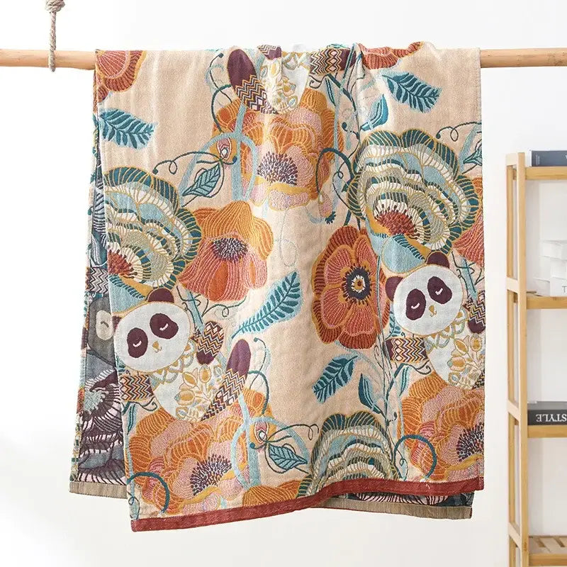 A soft beige decorbites boho cotton gauze bath towel featuring a vibrant floral and panda pattern in orange teal and brown