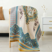 Beige boho cotton gauze bath towel with intricate blue teal and gold paisley patterns draped over wooden chair