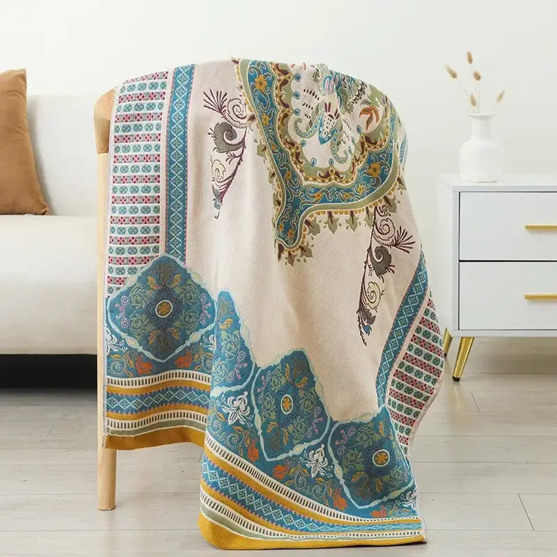 Beige boho cotton gauze bath towel with intricate blue teal and gold paisley patterns draped over wooden chair