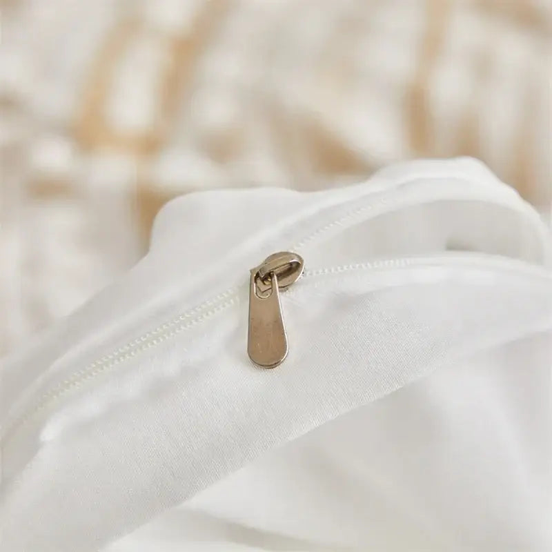 A sleek gold-toned zipper pull on soft white fabric of decorbites boho stripe pom pom duvet set
